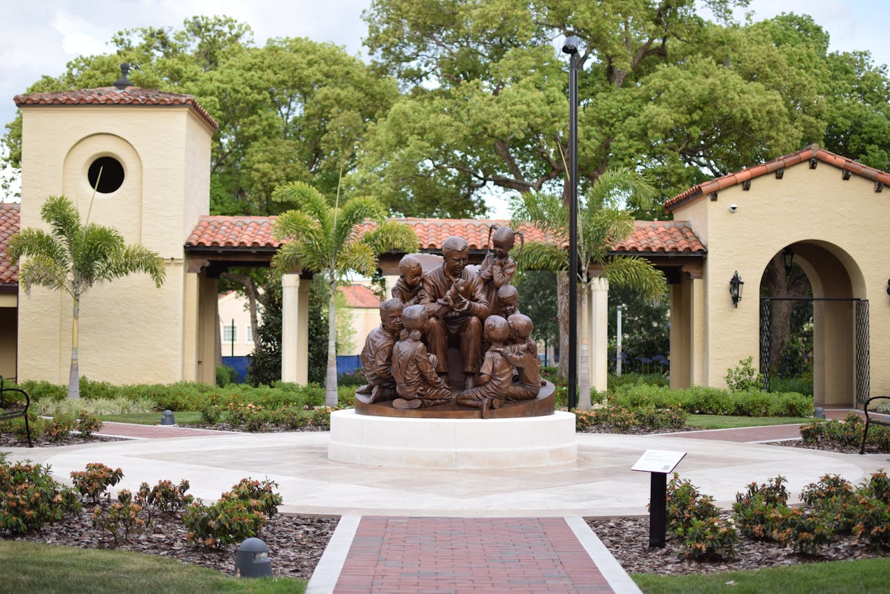 Bronze sculpture in a park setting surrounded by lush trees and architecture.