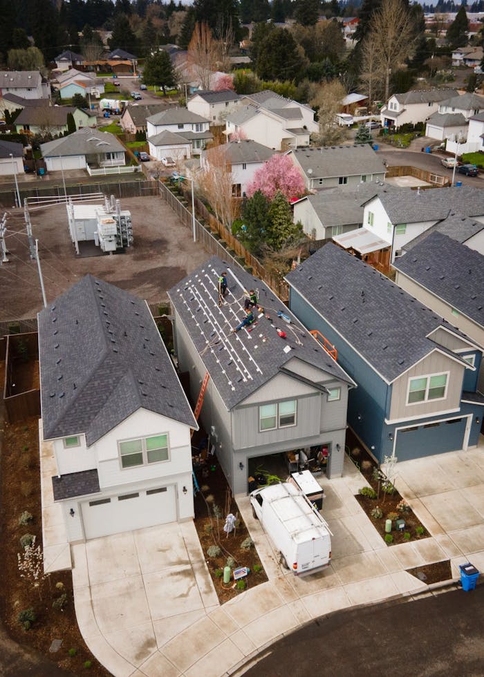 Drone shot of workers installing new roof panels in a suburban neighborhood.