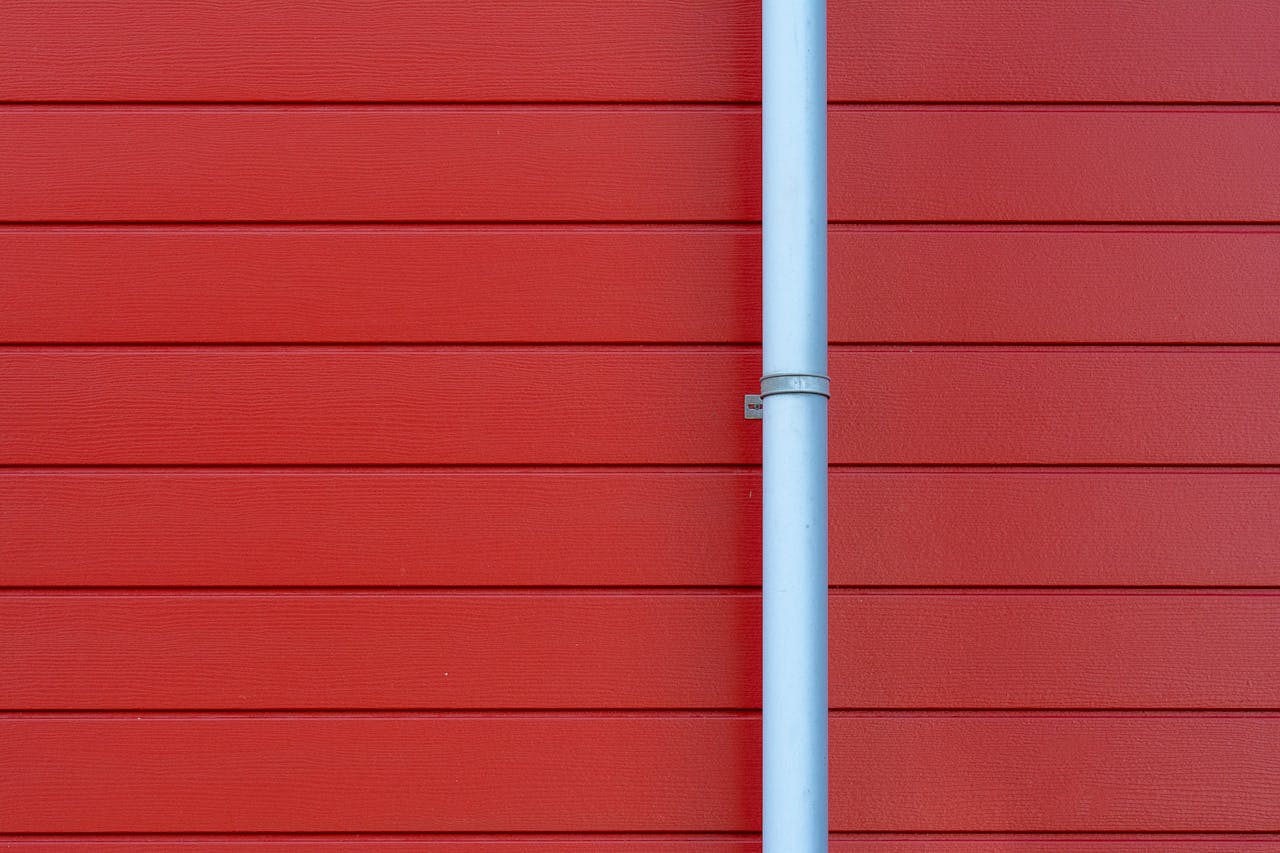 A minimalist photo of a red wall with a white rain gutter, showing clean lines and vibrant color contrast.